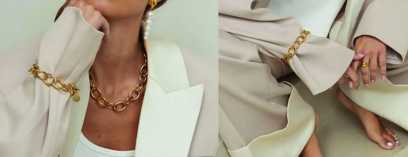 Gouden schakelketting, schakelarmband en pareloorbel op een crèmekleurig pak